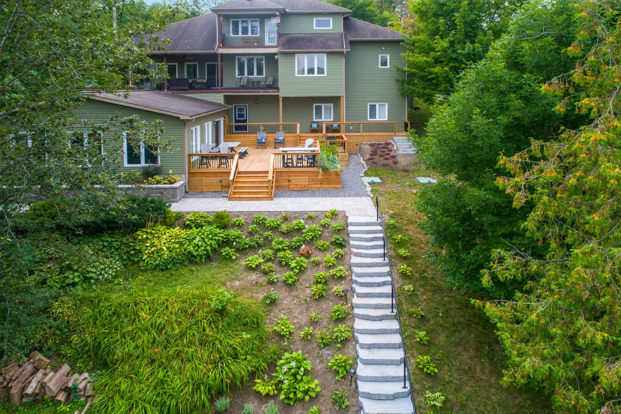 Elevated view of a wooded residential property showing decks, stairs, landscaping, and exterior conditions