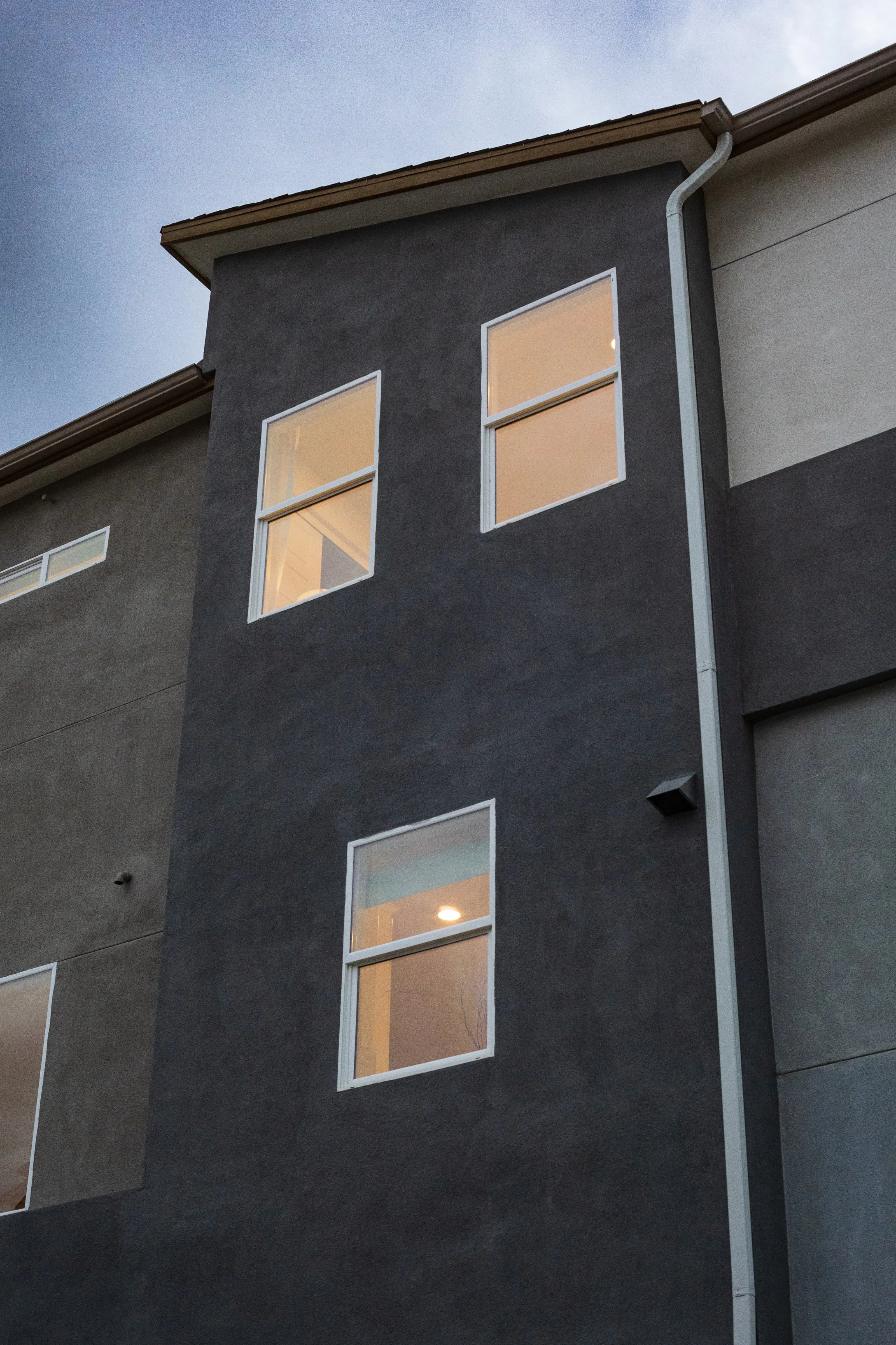 Geometric residential façade with illuminated windows and a visible downspout