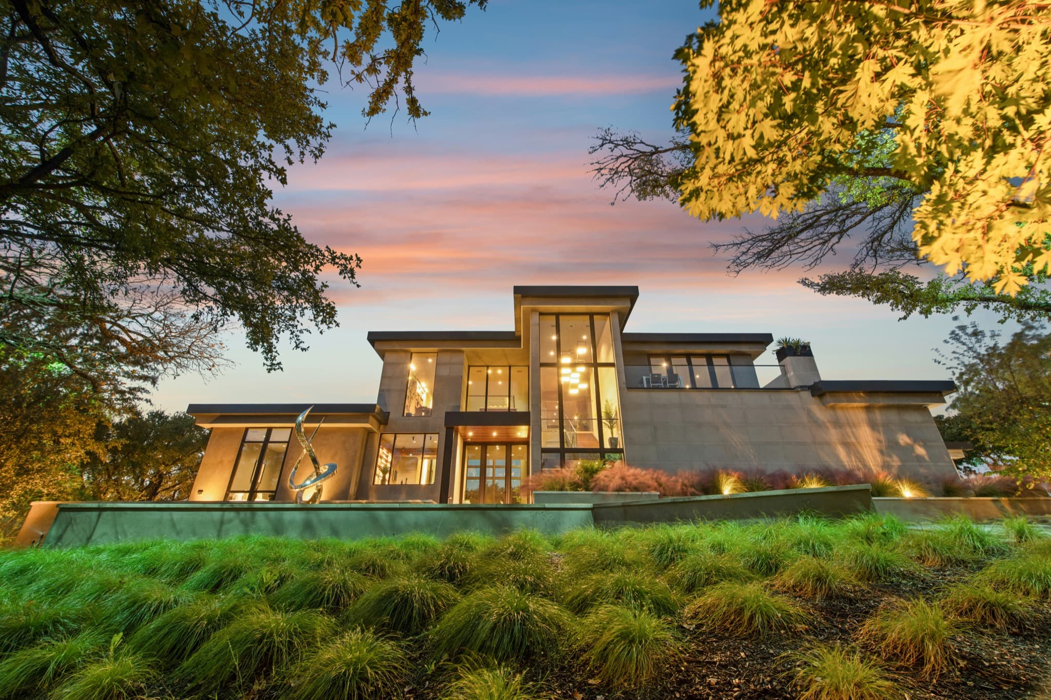 Contemporary home illuminated at dusk and surrounded by mature trees